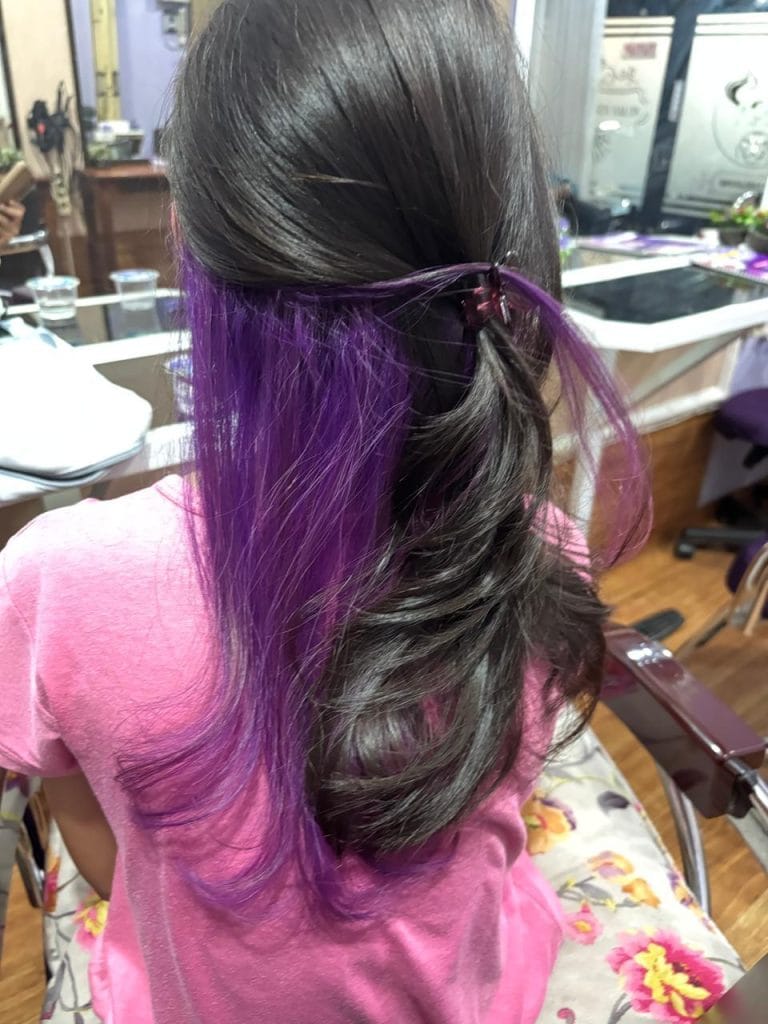 Hasil pewarnaan rambut teknik Peekaboo warna ungu vibrant pada bagian dalam rambut hitam di Claffa Salon