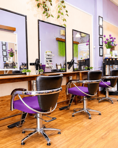 Sudut ruang styling Claffa Salon dengan deretan cermin rias besar, meja kayu, kursi hidrolik ungu, dan meja kasir resepsionis